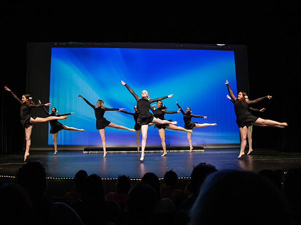 young women in elegant black dance outfits performing a ballet routine on stage